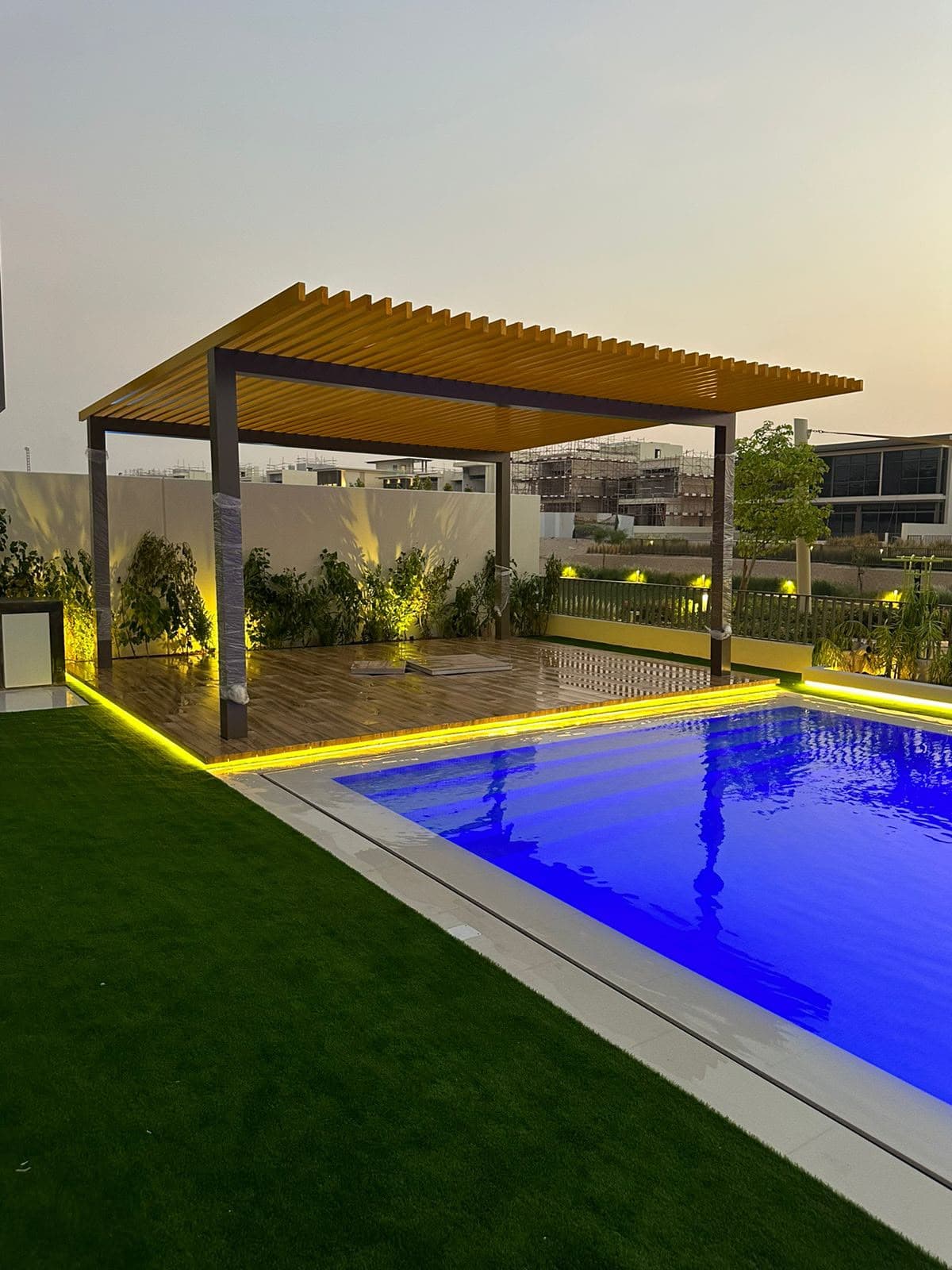Louvered aluminium pergola with LED lighting over an illuminated pool at dusk