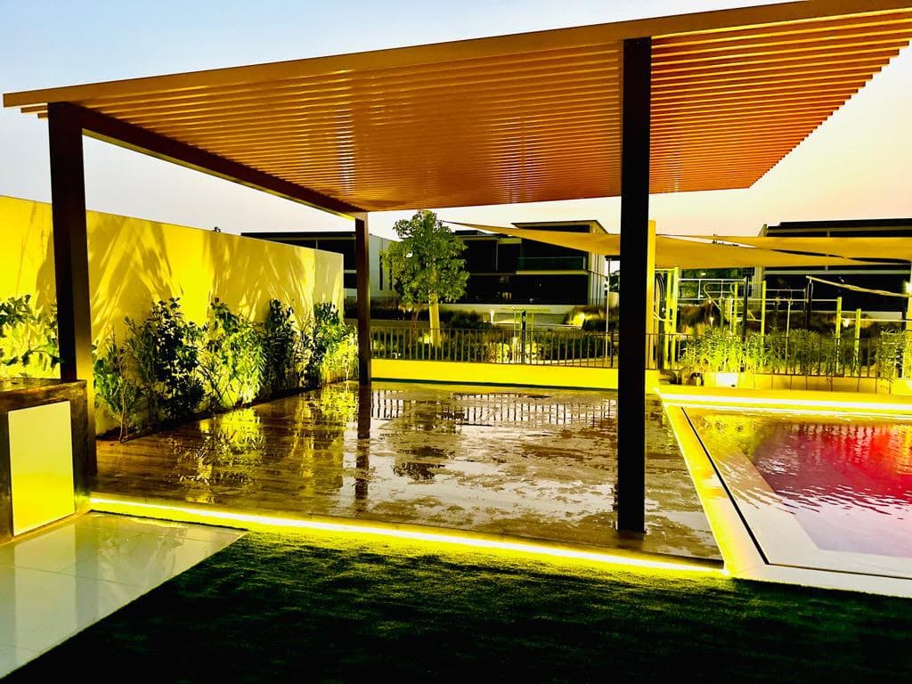Bamboo-slat pergola glowing beside a lit pool at dusk